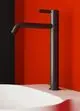 Schwarzes Standventil von Ideal Standard, mit geradem Auslauf und Lenkhebel, montiert an einem weißen Waschbecken vor rot-schwarzem Hintergrund.